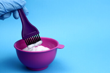 Mixing hair dye in plastic bowl. Hair coloring on a blue background