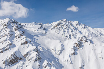 Winter snow mountains against blue sky and clouds from helicopter