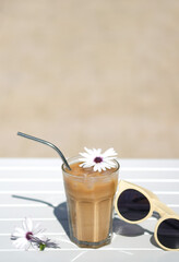 Ice coffee Cyprus Frappe Fredo top view on white table, with sunglasses. Summer minimalistic background, holiday or vacation concept. Sun and shadows.Copy space.