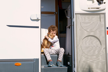 Fototapeta na wymiar boy of 4-5 years, Caucasian sitting in the motor home entrance in pajamas with his little puppy hugging him with affection and love