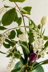 Beautiful spring bouquet on kenzane on lite background. White and purple tulips and branch of blooming bird cherry in ceramic vase. Simple floral still life