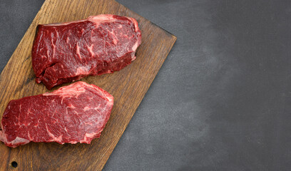 two raw pieces of beef steak on a brown wooden board, black tables