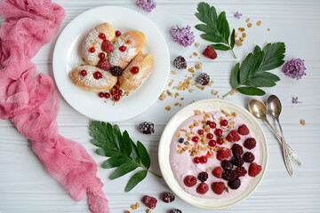 Top view of a plate with yogurt, berries and granola and a plate with croissants on a light background. Layout