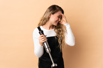 Young brazilian woman using hand blender isolated on beige background laughing