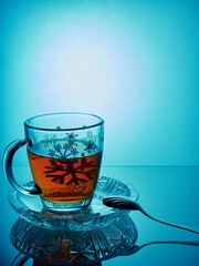 A mug of tea on a saucer and a teaspoon on the edge of the sauce.Mug of tea, on a blue background.On the mug painted snowflakes