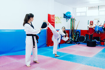 Two young women practice taekwondo in a training center