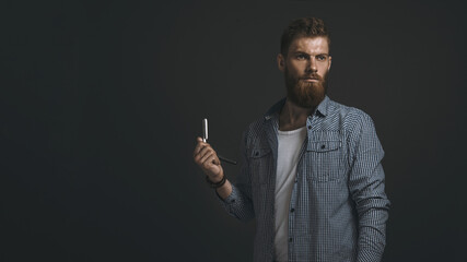 Portrait of brutal bearded man with straight razor in his hand. Copy space on left