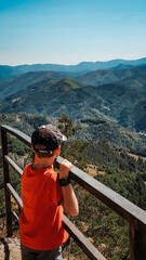 The boy admires the beautiful high-altitude landscape in the way of the road. Rest, hiking in the mountains, traveling. Vertical orientation.