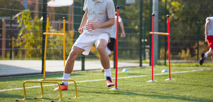 Teenage Football Players on Training Camp. Young Boys Running Slalom Track Between Training Poles and Jumping Over Hurdles. Soccer Training Equipment
