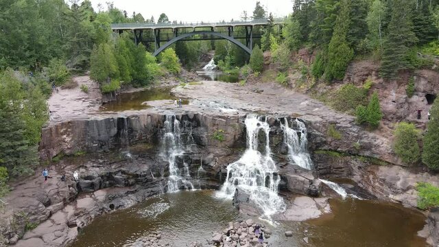 Aerial clip of Gooseberry waterfalls and highway overpass bridge. Waterfalls surrounded by rocky landscape and forested area. Near Duluth, MN. Outdoors, summer.