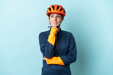 Young cyclist woman isolated on blue background having doubts and thinking