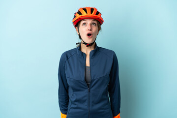 Young cyclist woman isolated on blue background looking up and with surprised expression