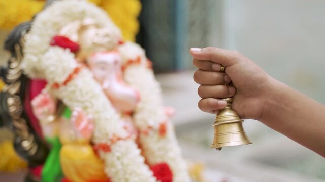 Close up of hand offering prayer by using Brass bell or Ghanti while worshipping lord Ganesha during festival