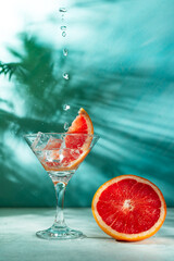 refreshing cocktail with grapefruit on a green background. a glass with ice and pieces of grapefruit is on the table in which the liquid is poured on top