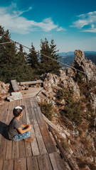 The boy sitting on the top of the mountain and admiring the view. Vertical