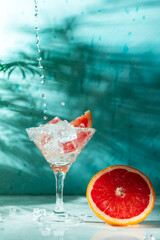 refreshing cocktail with grapefruit on a green background. a glass with ice and pieces of grapefruit is on the table in which the liquid is poured on top