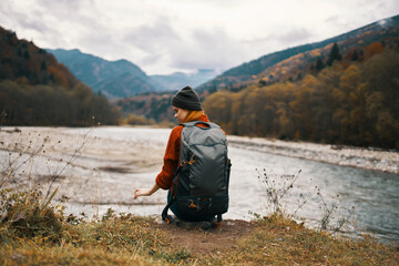 Fototapeta premium woman hiker on the banks of the river in autumn and mountains in the distance clouds weather nature
