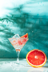 refreshing cocktail with grapefruit on a green background. a glass with ice and pieces of grapefruit is on the table in which the liquid is poured on top