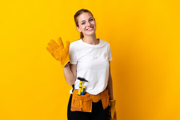 Young electrician woman isolated on yellow background saluting with hand with happy expression