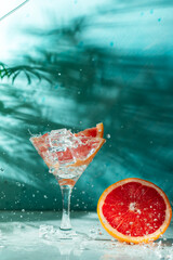 refreshing cocktail with grapefruit on a green background. a glass with ice and pieces of grapefruit is on the table in which the liquid is poured on top