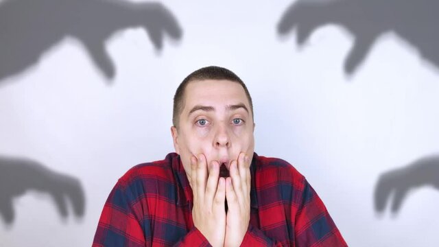 The man is experiencing a panic attack. The concept of phobia, fears, paranoia and persecution mania. Shadow silhouettes surrounded the man. Nervous breakdown and nervous disorders
