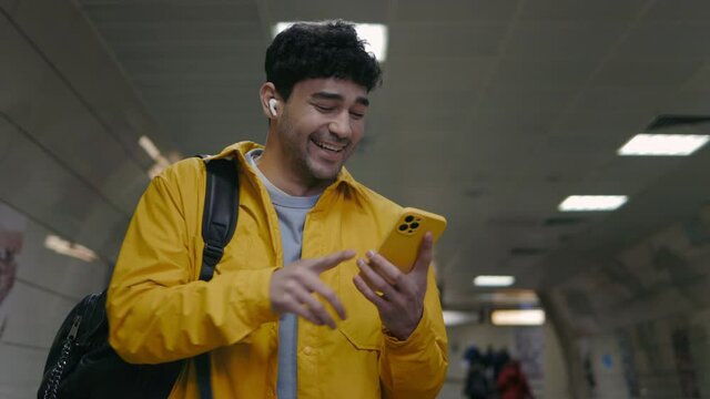Cheerful guy in earphones standing on escalator with mobile