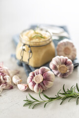 Fototapeta na wymiar Homegrown garluc bulbs in front of a glass jar full of fresh garlic paste laid on kitchen cloth with rosemary