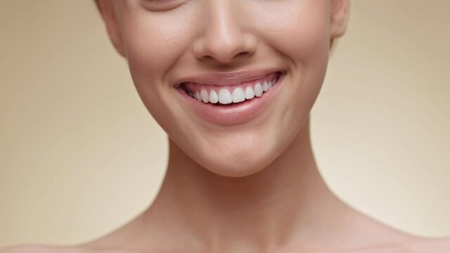 Closeup of woman smiling to camera, showing white smile of after teeth alignment procedure, beige background