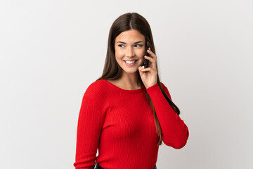 Teenager Brazilian girl using mobile phone over isolated white background looking to the side and smiling