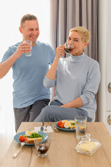 Healthy mature couple drink coffee at breakfast on a kitchen. Smiling, talking and laughing, wife looking at camera