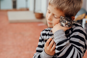 Kitten on the arm of the boy outdoors, child hugging his love pet. Children and domestic animals.