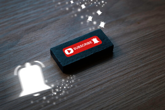 Wooden button with subscribe note and notification bell icon on wooden background. Motion blur of white notification bell. Concept of social media and digital online.