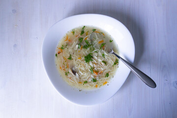 noodles with chicken in white bowl with spoon on wooden table