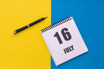 July 16th. Day 16 of month, calendar date. Notebook with a spiral and pen lies on a yellow-blue background