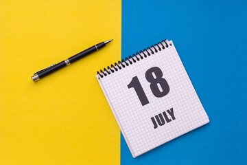 July 18th. Day 18 of month, calendar date. Notebook with a spiral and pen lies on a yellow-blue background