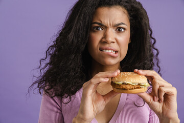 Young black woman with curly hair grimacing while eating hamburger