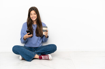 Young woman sitting on the floor holding coffee to take away and a mobile