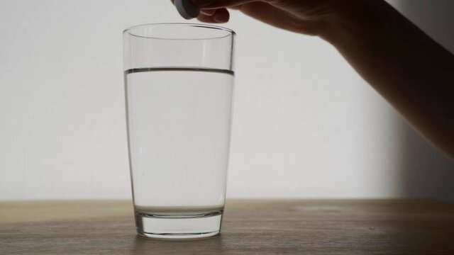 A woman throws a pill into a glass of water. Effervescent tablet dissolves in a glass of water close-up. Slow motion, HD.