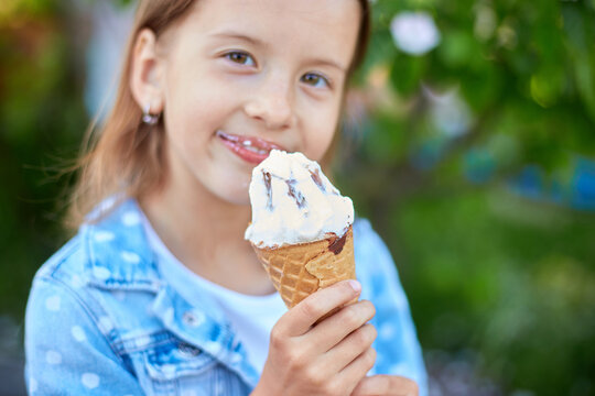 Cute girl with italian ice cream cone smiling and looking at camera while resting in park on summer day, child enjoying ice cream outdoor, happy holidays, summertime