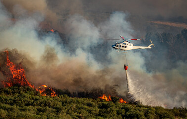 Helicopter with bambi bucket over the fire