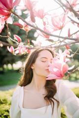 Woman enjoys and sniffs magnolia flowers in spring garden.