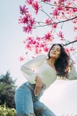Woman poses near blooming magnolia tree against sky background.