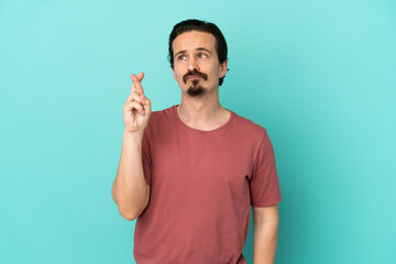Fototapeta premium Young caucasian man isolated on blue background with fingers crossing and wishing the best