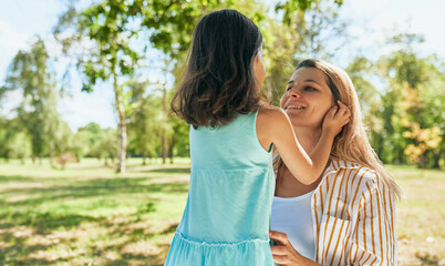 Naklejka premium Rear view of happy mother and her joyful little girl playing in the park during the picnic. Joyful young woman and daughter smiling and spending time together on a sunny day. Mother's day concept.