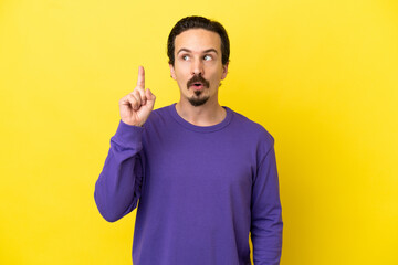 Young caucasian man isolated on yellow background thinking an idea pointing the finger up