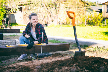 Young woman doing construction work in country house garden using building level