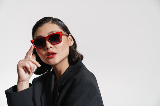 Brunette asian woman wearing jacket and sunglasses looking at camera