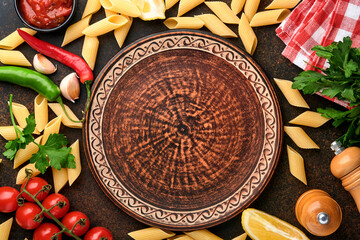 Pasta background. Pasta rigati, tomato ketchup sauce, olive oil, spices, parsley, and fresh tomatoes on a dark slate table. Food cooking background. Top view with copy space.