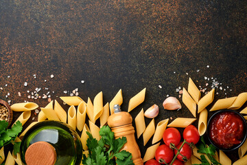 Pasta background. Pasta rigati, tomato ketchup sauce, olive oil, spices, parsley, and fresh tomatoes on a dark slate table. Food cooking background. Top view with copy space.