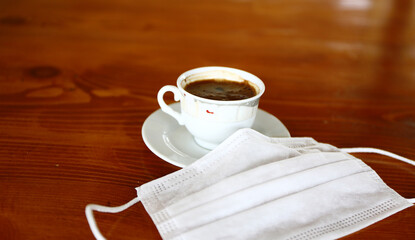 White colored coffee cup of serving style arabica coffee in Turkey, Greece, Cyprus, North Africa and Middle East. And protective face mask next to sevice.
